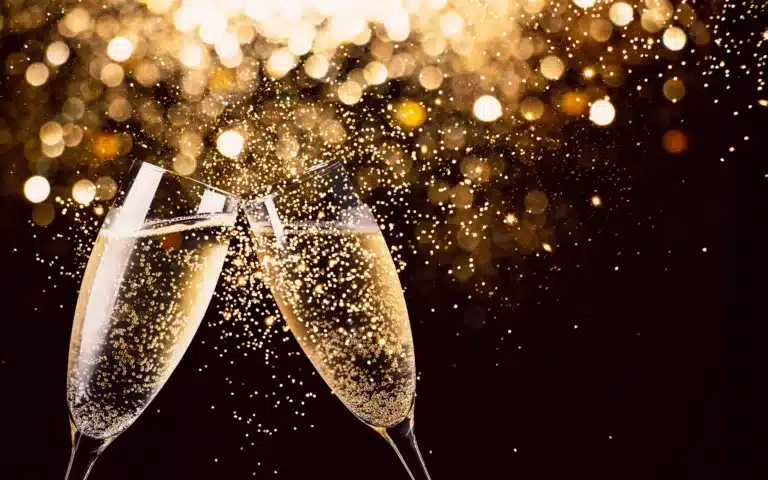 New Year's Eve – Two glasses of champagne toasting in the nigh with lights bokeh, glitter and sparks on the background